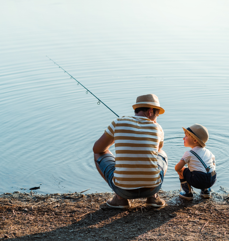 This is a father and son fishing along the coast. Both are wearing straw hats that shield their faces from the sun. 